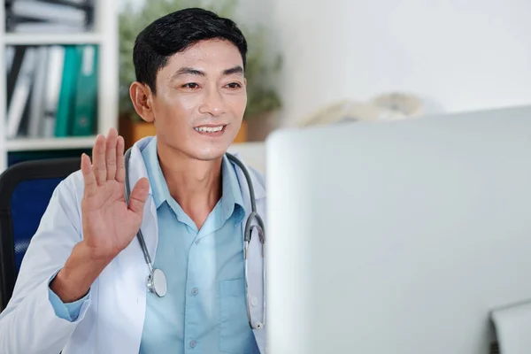 在网上会议上同同事打招呼时 微笑着与成熟的全科医生握手 — 图库照片