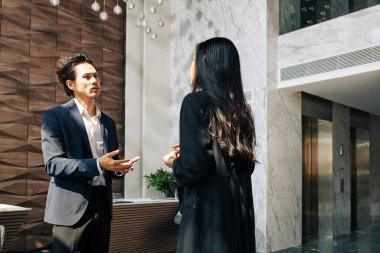 Ciddi bir melez işadamı ofis binasının lobisinde kadın girişimciyle konuşuyor.