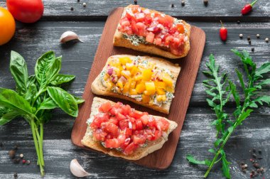 Peynir kırmızı ve sarı domates Bruschetta. Kompozisyon fesleğen, roka, biber ve sebze yaprakları ile dekore edilmiştir. Eski bir ahşap zemin üzerine üstten görünüm.
