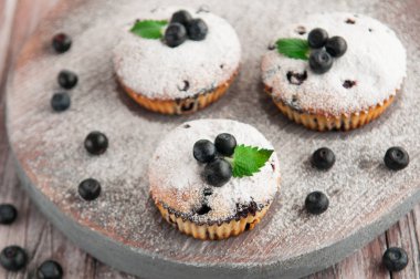 Pudra şekeri, yaban mersini ve nane ile dekore blueberry muffins. Ahşap arka plan üzerinde bir rustik tarzda fotoğraf. Bulanık.