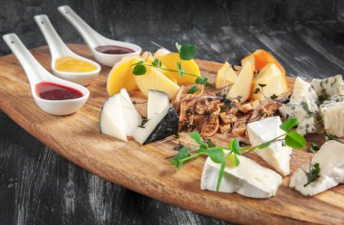 Karanlık bir arka plan üzerinde peynir tabağı. Taze ot ve incir ile dekore edilmiştir. Arka plan bulanık