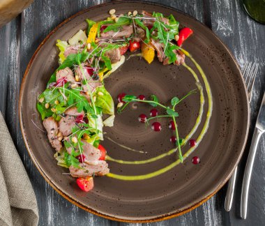 Roka sebze, çam fıstığı ve portakal soslu ördek salatası. Üstten görünüm koyu ahşap arka plan üzerinde.