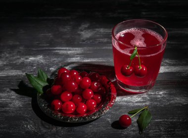Bardakta vişne suyu. Kirazlarla süslenmiş. Koyu ahşap ba