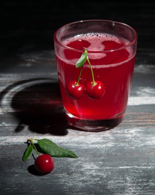 Bardakta vişne suyu. Kirazlarla süslenmiş. Koyu ahşap ba