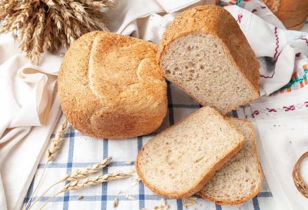 Хлеб с отрубями. На белой полосатой скатерти. На скатерти два нарезанных куска хлеба, колосья пшеницы и зерна. Вид сверху. Кантри стиль . — стоковое фото