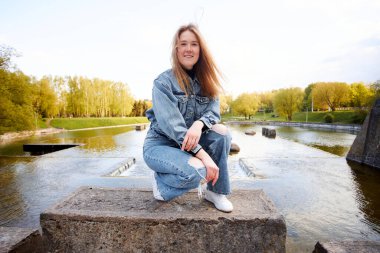 90 'ların kızıl saçlı güzel portresi. İskandinav genç kız. Parkta gölün kenarında kot pantolon giymiş..