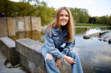 90 'ların kızıl saçlı güzel portresi. İskandinav genç kız. Parkta gölün kenarında kot pantolon giymiş..