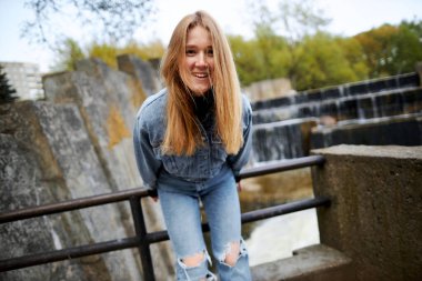 90 'ların kızıl saçlı güzel portresi. İskandinav genç kız. Parkta gölün kenarında kot pantolon giymiş..