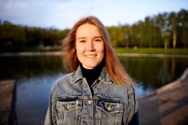 90 'ların kızıl saçlı güzel portresi. İskandinav genç kız. Parkta gölün kenarında kot pantolon giymiş..