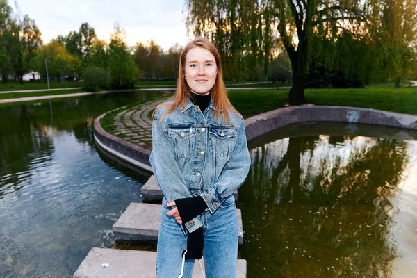 Flash photo of a beautiful redhead girl in 80s jeans in a park near the water.