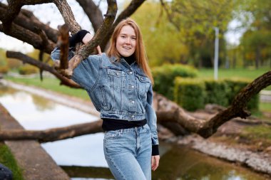 Parktaki dallı bir ağacın yanında kızıl saçlı gülümseyen bir kızın güzel portresi..