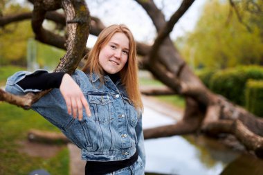 Parktaki dallı bir ağacın yanında kızıl saçlı gülümseyen bir kızın güzel portresi..