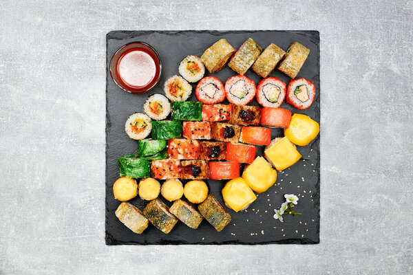 Fresh fish sushi set with side dishes on a black graphite board and gray background.
