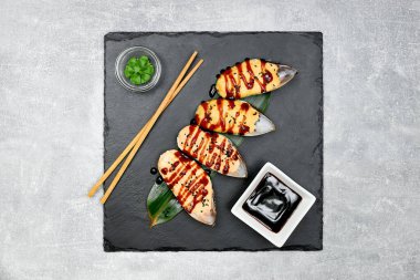 4 adet soya soslu fırında midye, wasabi ve yemek çubukları siyah bir grafit tahtası ve gri arka planda..