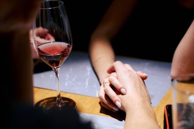 Erkek ve kadın, romantik bir akşam yemeğinde şarap eşliğinde el ele verdiler..