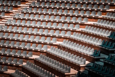 Birden çok satır ücretsiz sahipsiz koltuklarda. Boş genel arena ve konser amfitiyatro günbatımı fotoğrafı. Kırmızı tuğla ve Beyaz Traverten yapısı, gri plastik sandalye. 