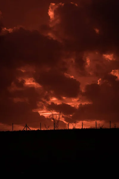可怕的日落 有红色的天空和云 暴风雨过后 电力塔架 电池塔和有线围栏后面的金属结构 在一个被破坏的景观 恶劣的环境 — 图库照片