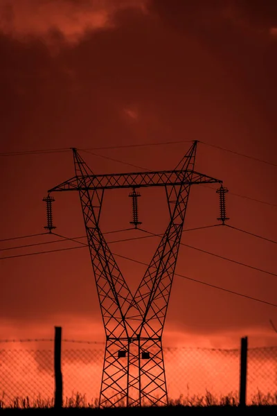 Scary sunset, with red sky and clouds, after the storm. Power pylons, cell towers and metal structures behind wired fences. Pollution, in a devastated landscape. Evil environment.