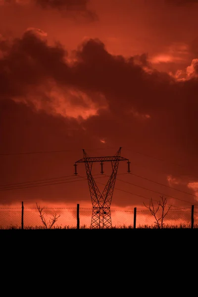 赤い空と雲 嵐の後の恐ろしい日没 携帯基地局や有線のフェンスの後ろに金属構造物 荒廃した風景の中 悪環境 — ストック写真