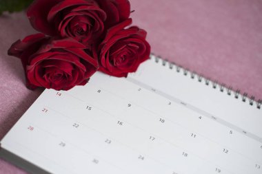 Takvim ve üç kırmızı gül yalan üzerine bir pembe, pembe bir arka plan üzerinde sayılar yalan ile bir Takvim Takvim kırmızı gül yalan