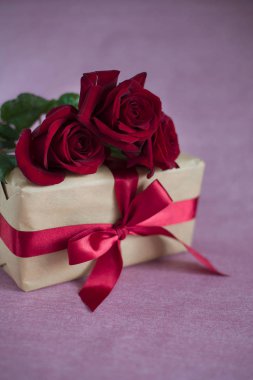 kutusu bağlı kırmızı kurdele, pembe bir arka plan üzerinde üç kırmızı gül ile (dikey olarak kapat)