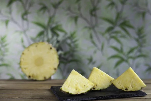 triangular pineapple slices on slate dish and half pineapple on  vegetation and wood background