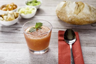 Spanish Cuisine Gazpacho. Andalusian cold soup served in a glass with garnish bowls, bread, napkin and spoon on wooden table clipart