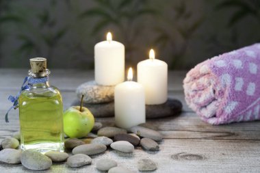 şişe elma yağı masaj, nehir çakıl taşları, küçük bir yeşil elma, havlu ve ahşap masa ve bitkisel arka plan üzerinde üç yanan mumlar 