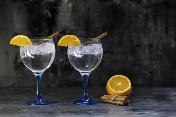 蓝色玻璃上的两个杜松子酒，有肉桂和橙子 — 图库照片