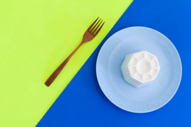 Mavi tabakta taze İspanyol peyniri ve mavi ve sarı arka planda çatal.