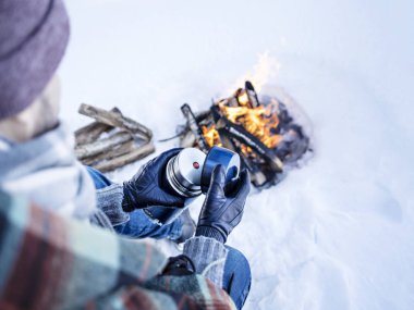 Adam içki ile termos sahip kış kamp ateşi.