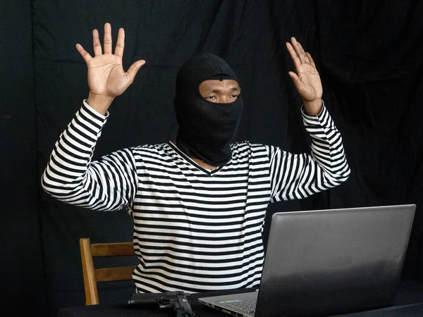 computer hacker caught in the act of cyber crime.Portrait of baffled hacker raising hands to surrender to the police.