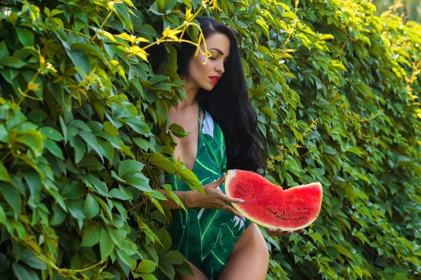 sensual brunette woman in green swimsuit with watermelon in hand