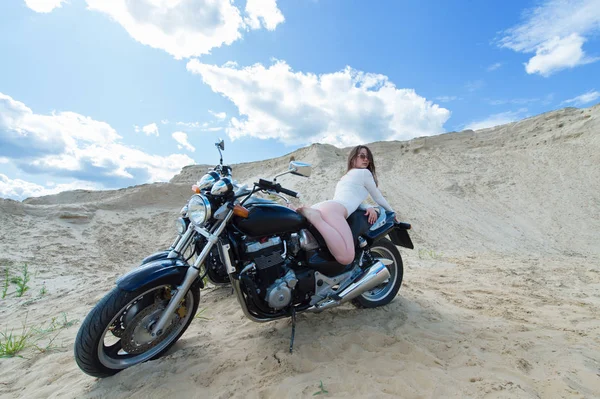 attractive sensual woman lies on motorcycle among the sands