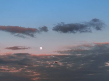 Arka planda dolunay ile gün batımı gökyüzü üzerinde uçan uçak