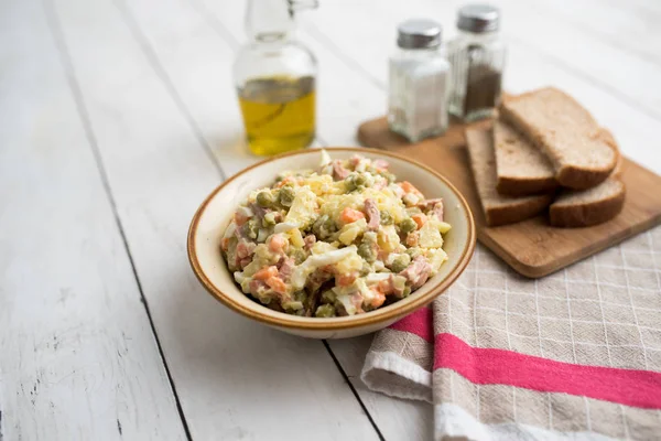 Bowl of traditional Russian salad called Olivie, Russian New Year or Christmas salad on wooden background. Salad from cooked vegetables. Potato salad.