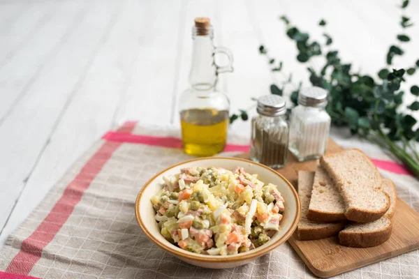 Bowl of traditional Russian salad called Olivie, Russian New Year or Christmas salad on wooden background. Salad from cooked vegetables. Potato salad.