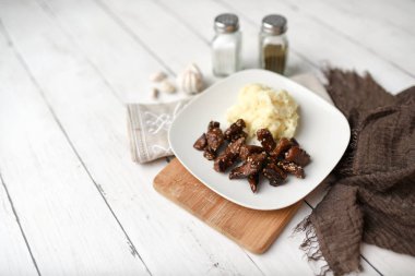 Beyaz ahşap zemin üzerinde susamlı biftek tabağı patates püresi ve baharatlarla servis edilir.