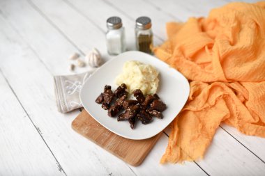 Beyaz ahşap zemin üzerinde susamlı biftek tabağı patates püresi ve baharatlarla servis edilir.