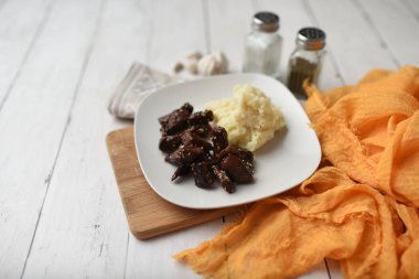 Beyaz ahşap zemin üzerinde susamlı biftek tabağı patates püresi ve baharatlarla servis edilir.