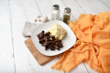 Beyaz ahşap zemin üzerinde susamlı biftek tabağı patates püresi ve baharatlarla servis edilir.