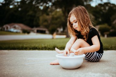 Kaldırıma tebeşirle çizen küçük kız. Evdeki küçük çocuklar için karantina hayatı aktif hale geliyor..