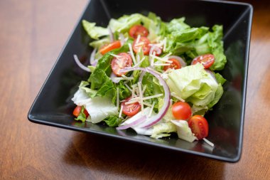 Siyah bir kasede salata. Peynirli ve soğanlı marullu vişneli domates.