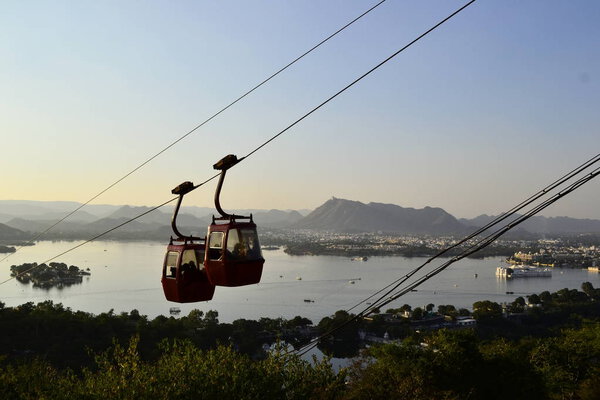 Two hanging cabins of Mansapurna Karni Mata Ropeway and panoramic view to the Pichola Lake with clear blue sky, Udaipur, Rajasthan, India