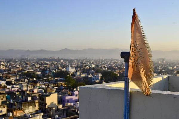 Orange flag with the Om hinduism symbol. Cityscape of Udaipur town in the morning from roof top and mountain range on a horizon. Rajasthan, India