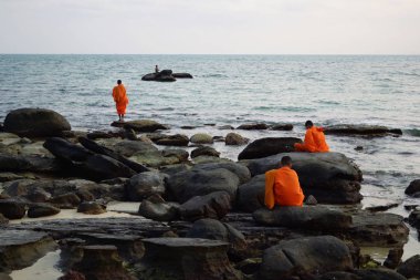 Üç Budist keşiş turuncu elbiseler (geleneksel giyim) Sihanoukville, Kamboçya deniz yakınındaki kayalar üzerinde günbatımı zevk