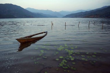 Eski ahşap tekne Pokhara Phewa Gölü üzerinde suya yansıyan. Sakin ve sabah havasında rahatlayın. Bir arka planda Annapurna dağ aralığı 