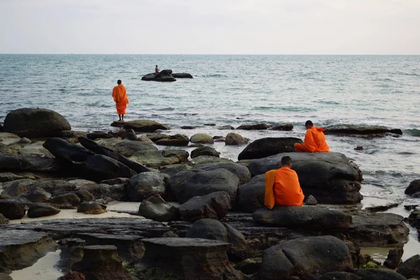 Üç Budist keşiş turuncu elbiseler (geleneksel giyim) Sihanoukville, Kamboçya deniz yakınındaki kayalar üzerinde günbatımı zevk
