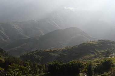 Pirinç terasları ve alanları ile vadi üzerinde güneş ışınları. Tepelerin üzerinde güneş ışınları. Güneşli parlak hava ile çarpıcı dağlar manzara. Güneş ışınları bulutlu gökyüzünde parlıyor. Sa Pa, Vietnam