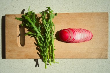 Taze arugula dilimlenmiş turp o kesme tahtası ile bırakır. Rucola ve turp ile bahar taze salata pişirme. Üstte görüntü.